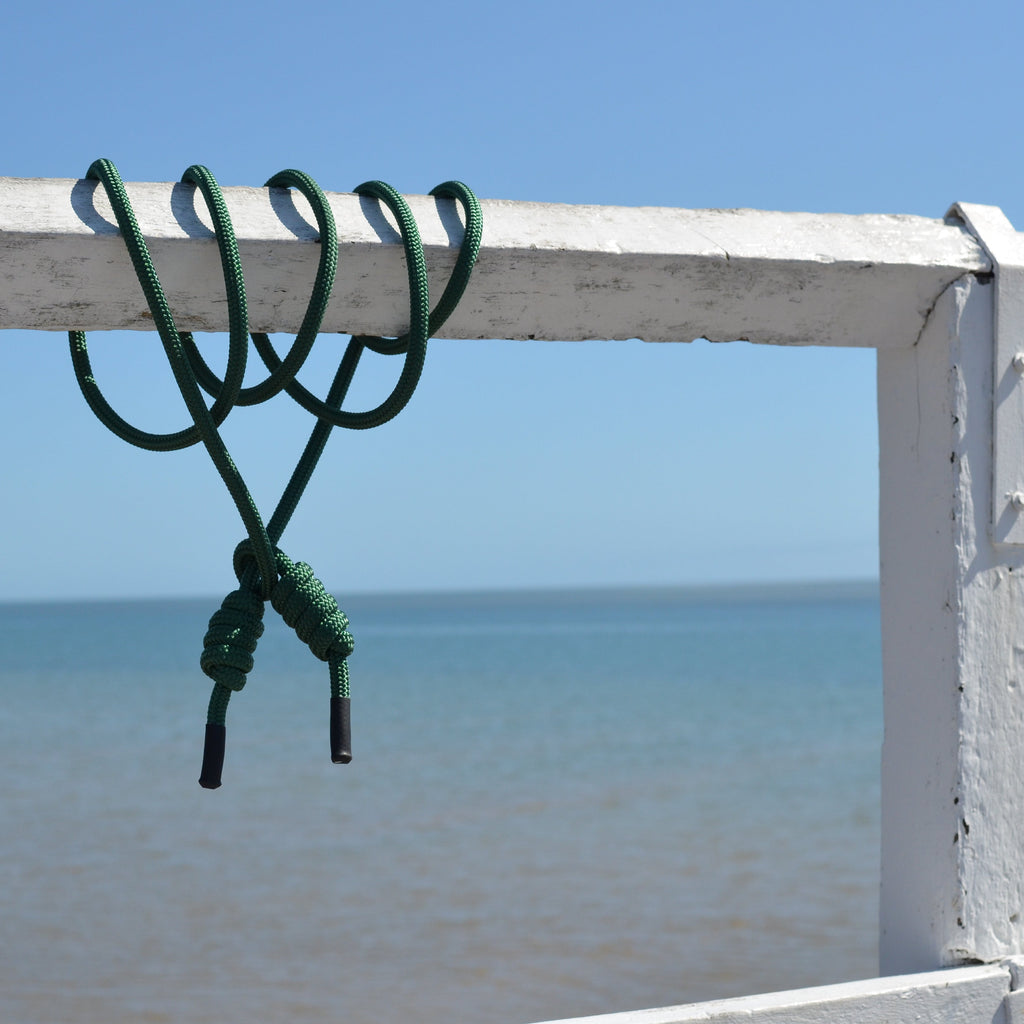 A green flow rope wrapped around a white painted wooden railing, with an ocean and blue sky background.